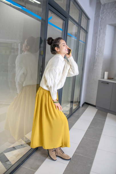 Young woman leaning on glass wall, talking on mobile phone - 写真・画像