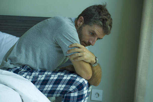dramatic portrait of attractive scared and depressed 40s man on bed in pajamas feeling worried suffering anxiety and depression problem during virus quarantine home lockdown - Фото, зображення