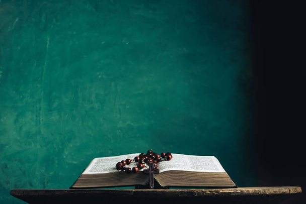 Offene Bibel und Perlenkreuz auf einem alten runden Holztisch. Schöne grüne Wand Hintergrund. - Foto, Bild