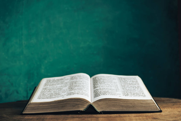 Otwórz Biblię na starym okrągłym drewnianym stole. Piękne zielone tło ściany. - Zdjęcie, obraz