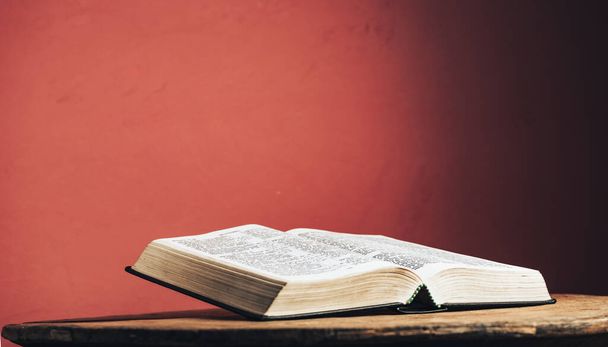 Ανοίξτε την Αγία Γραφή σε ένα παλιό καφέ στρογγυλό ξύλινο τραπέζι. Όμορφο φόντο κόκκινο τοίχο. - Φωτογραφία, εικόνα