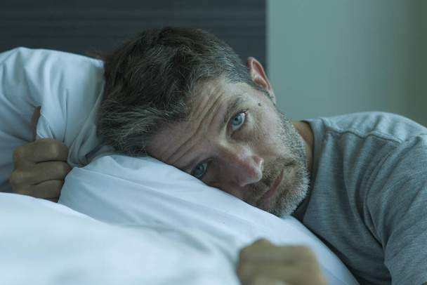 dramatic portrait of attractive scared and depressed 40s man on bed in pajamas feeling worried suffering anxiety and depression problem during virus quarantine home lockdown - Photo, image