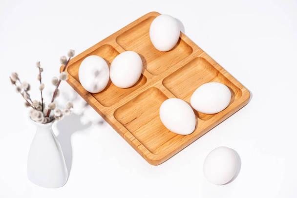 Primavera Pascua naturaleza muerta. Huevos de Pascua y ramitas de sauce en un jarrón blanco sobre una superficie blanca. Vista superior
. - Foto, Imagen