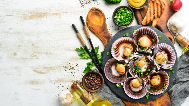 Baked scallops in seashells with garlic and spices on a black stone plate. Seafood. Top view. Free space for text. - Photo, Image