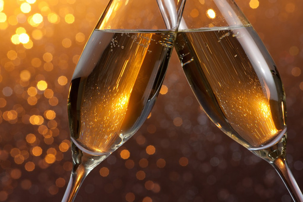 detail of a champagne flutes with golden bubbles on orange light bokeh background - Foto, afbeelding