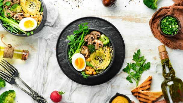 Buddha bowl: avocado, chickpeas, mushrooms, egg and arugula in a black bowl. Top view. Free space for text. - Foto, Imagem