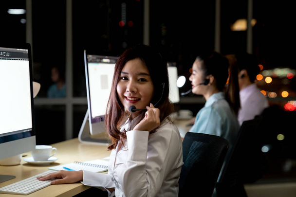 Asian young adult confidence operator colleague team with headsets working in a call center at night as customer service and technical support. Using as Late night hard working 24 Hr. 7 Days concept. - Foto, Imagem