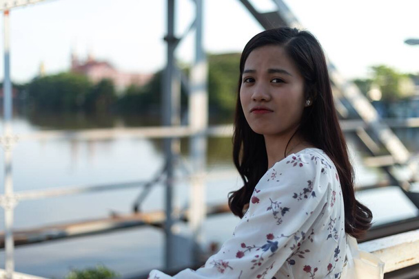 A black-haired Vietnamese girl on a bridge  showing the emotion of concern and sadness - Photo, Image