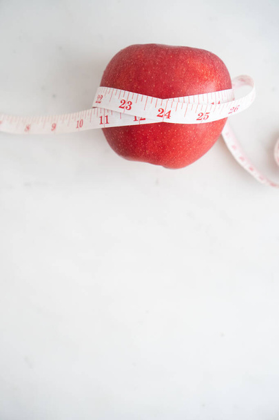 Pomme enveloppée avec du ruban à mesurer sur une surface en marbre blanc. Concept de nutrition fruitière et diététique
. - Photo, image