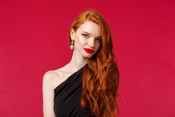 Κοντινό πλάνο πορτρέτο της ελκυστική αισθησιακή και flirty νεαρή γυναίκα με κόκκινο κραγιόν, συλλαμβάνοντας το βλέμμα, φορούν σκουλαρίκια και μαύρο φόρεμα, κοίτα κάμερα αυθάδης ξέρει τι θέλει, κόκκινο φόντο - Φωτογραφία, εικόνα