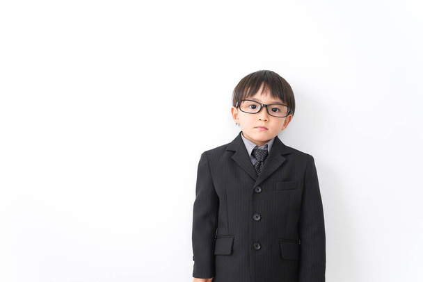 Stüdyoda beyaz arka planda poz veren takım elbiseli ve gözlüklü küçük çocuk. - Fotoğraf, Görsel