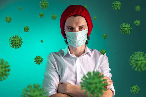 Portrait of a young man in a medical mask surrounded by COVIND-2019 coronavirus on a green background. Protection and threat during a pandemic and epidemic in 2020. - Foto, Bild