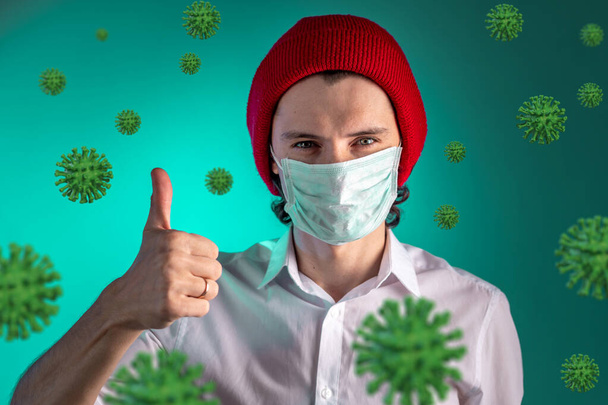 Portret van een jonge man met een medisch masker omringd door COVIND-2019 coronavirus op een groene achtergrond. Bescherming en bedreiging tijdens een pandemie en epidemie in 2020. - Foto, afbeelding