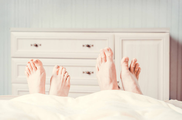 The feet of young couple peeking out from the blanket. Cozy morning in comfortable bed.  - Photo, Image