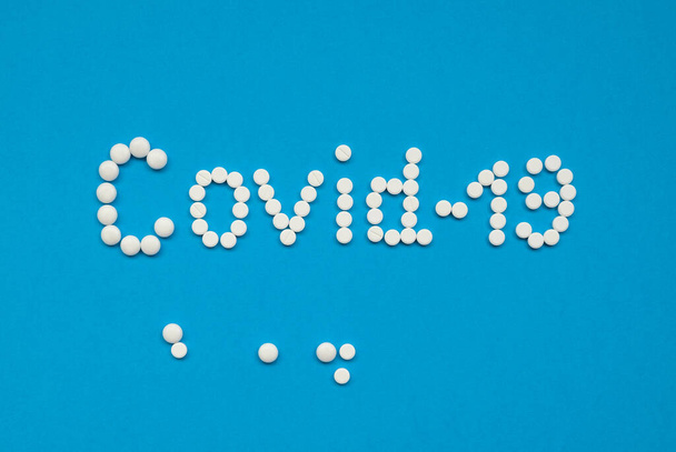 Le mot COVID-19, disposé avec des comprimés blancs sur fond bleu horizontalement
. - Photo, image