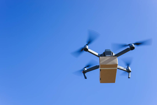 летающий беспилотник с коробкой на фоне голубого неба, доставка беспилотника - Фото, изображение