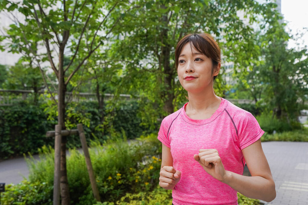 portrait of sporty Asian woman jogging in summer park  - Фото, изображение