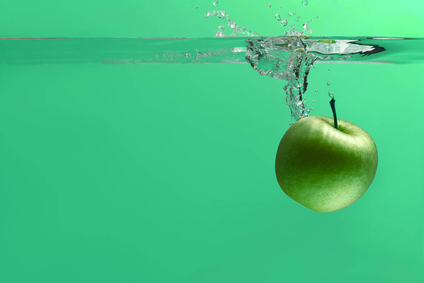 green apple falls into an aquarium with water on a green background - Foto, Bild