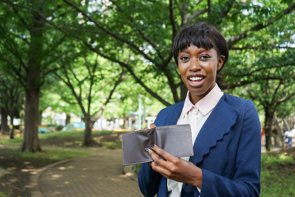 jong Afrikaans zakenvrouw houden portemonnee in park - Foto, afbeelding