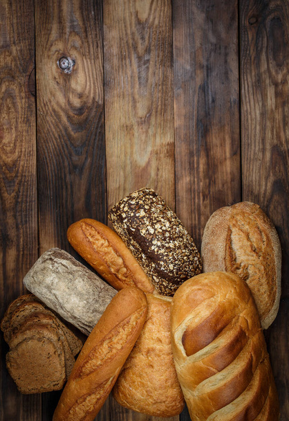Different loaves of bread and rolls with wheat and flour on a wooden table - Photo, Image