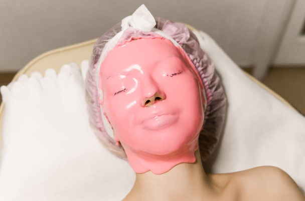 Woman Skin Care. Closeup Of Beautiful Girl With Cosmetic Mask On Facial Skin In Beauty Salon. Young Female With Face Covered With pink Moisturizing Alginate Mask. Beauty Treatment.  - Photo, Image