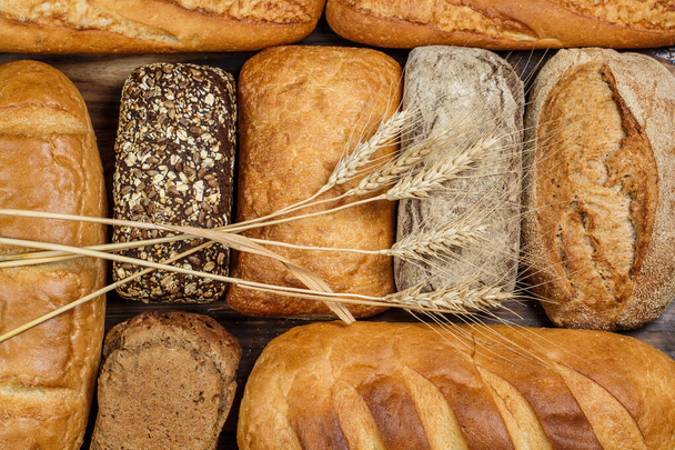 Různé bochníky chleba a rolky s pšenicí a moukou na dřevěném stole - Fotografie, Obrázek