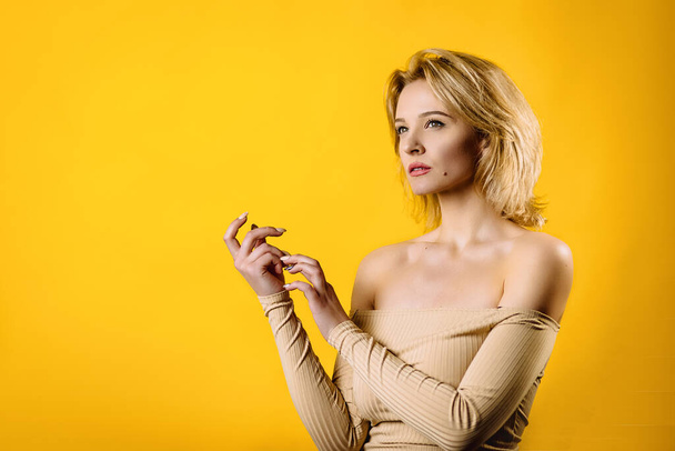Portrait of attractive young model with blonde hair on yellow background. girl posing in the studio. focus on hands - Foto, Bild