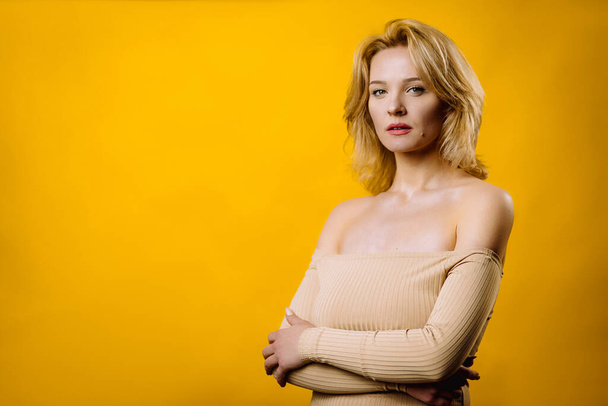 Young beautiful blonde woman over yellow background serious expression on face with crossed arms. - Foto, Imagem
