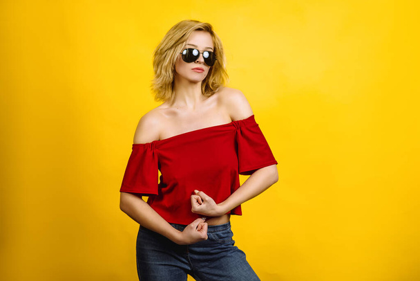 beautiful woman in sunglasses posing hands. blonde in a red top. young woman shows muscles joking - Foto, Bild