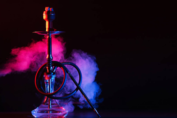 glass hookah shisha with a metal bowl on the table on a black background with smoke - Photo, Image