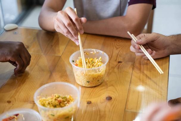 Détail des mains d'un groupe de jeunes de différentes ethnies partageant la nourriture asiatique dans un restaurant - Photo, image