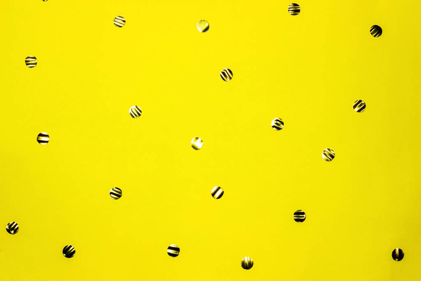 Золотые круглые конфетти на желтом фоне. Праздничный фон. Вид сверху, плоский
. - Фото, изображение