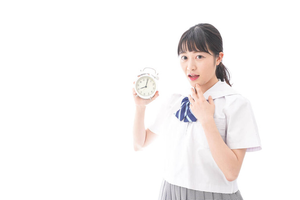 retrato de mujer joven asiática en uniforme escolar sosteniendo reloj despertador aislado sobre fondo blanco
 - Foto, imagen