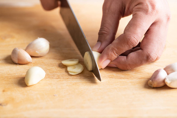 Рука тримає кухонний ніж і рубає часник на дерев'яній дошці для приготування їжі
 - Фото, зображення