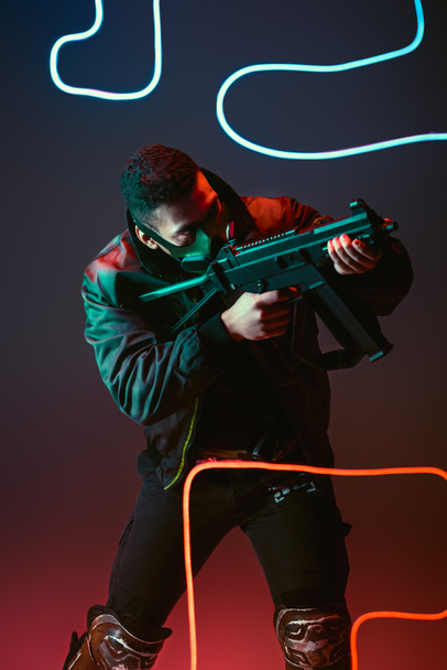 hombre bi-racial cyberpunk en máscara protectora apuntando pistola cerca de la iluminación de neón en negro
  - Foto, imagen