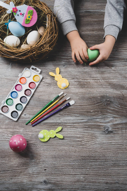 baby hand turn easter egg. In wooden table paints, brushes, bunny, nest. Prepares to paint Easte eggs - Fotografie, Obrázek