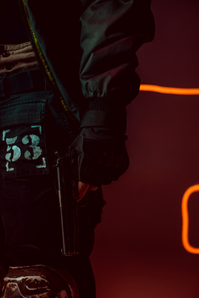 oříznutý pohled na kyberpunkového hráče s pistolí na černém s neonovým osvětlením  - Fotografie, Obrázek