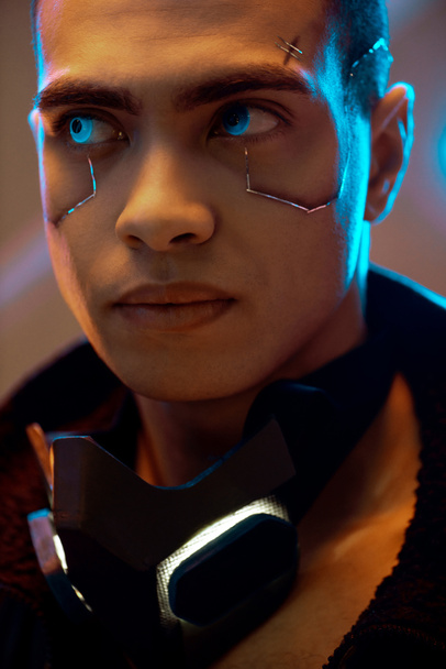 Cyberpunk-Spieler mit Metallic-Platten im Gesicht, der in der Nähe von Neonlicht wegschaut  - Foto, Bild