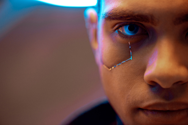 bijgesneden weergave van gemengde ras cyberpunk speler met metalen platen op gezicht en blauwe ogen op zoek naar camera - Foto, afbeelding
