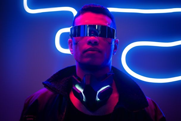 jugador cyberpunk de raza mixta en gafas futuristas cerca de la iluminación de neón azul
  - Foto, Imagen