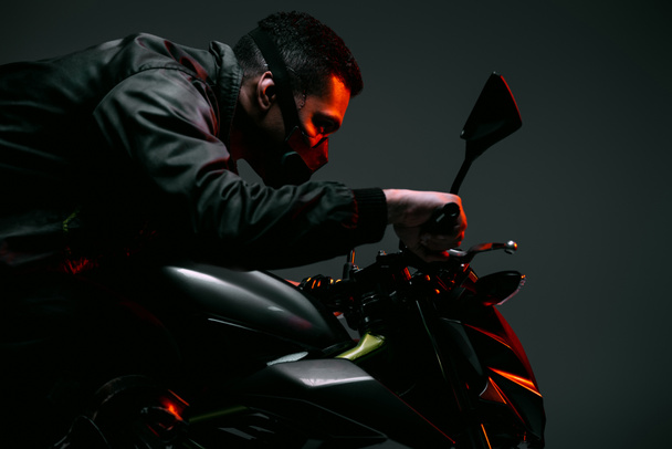 profile of mixed race cyberpunk player in mask riding motorcycle on grey  - Foto, imagen