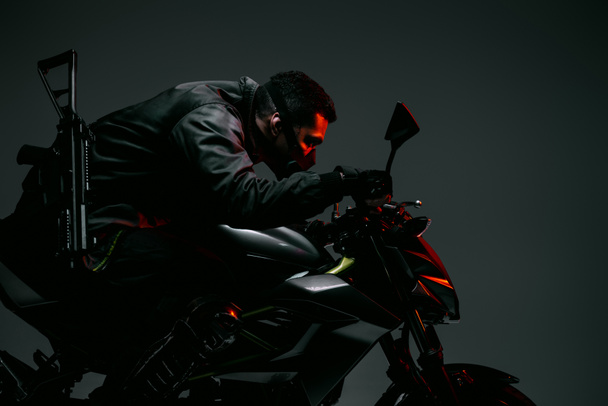 perfil del jugador de cyberpunk bi-racial armado en la máscara que monta la motocicleta en gris
  - Foto, Imagen