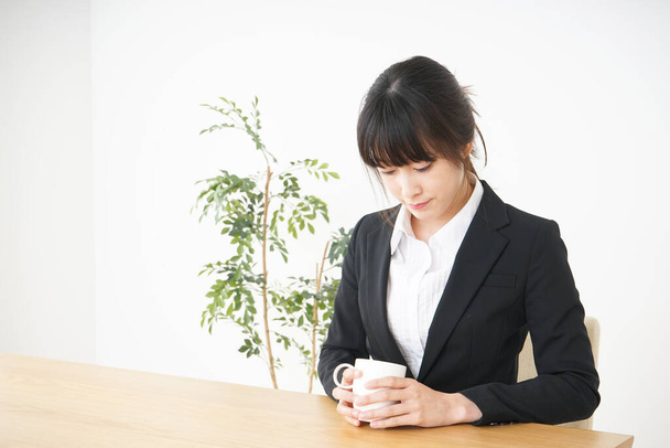 young Asian businesswoman with cup of tea in office  - Fotó, kép