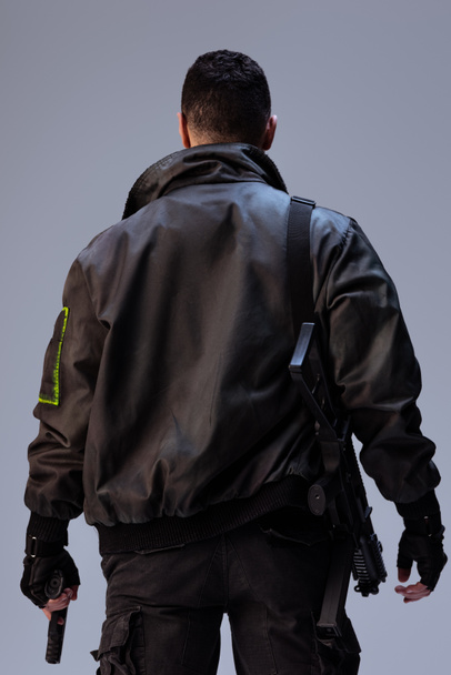 Rückansicht des Cyberpunk-Spielers mit Waffe im Stehen auf grau   - Foto, Bild