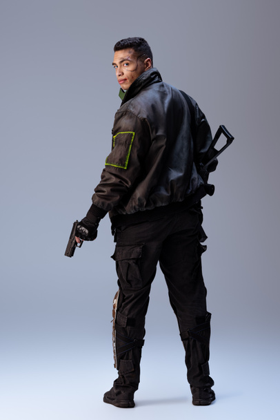 mixed race cyberpunk player holding gun and standing on grey   - Φωτογραφία, εικόνα