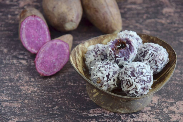 Клепон Ubi Ungu, фиолетовый сладкий картофель глютиновые рисовые шарики фаршированные пальмовым сахаром с покрытием на пару высушенный кокос. Деревянный фон - Фото, изображение