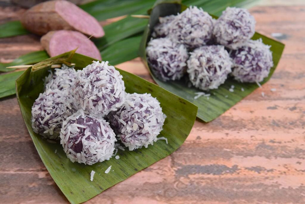 Клепон Уби Унгу, индонезийский традиционный десерт или Джаджанан Пасар. Пурпурный сладкий картофель глютиновые рисовые шарики, фаршированные пальмовым сахаром, покрытые высушенным на пару кокосом. Подается на банановом листе - Фото, изображение