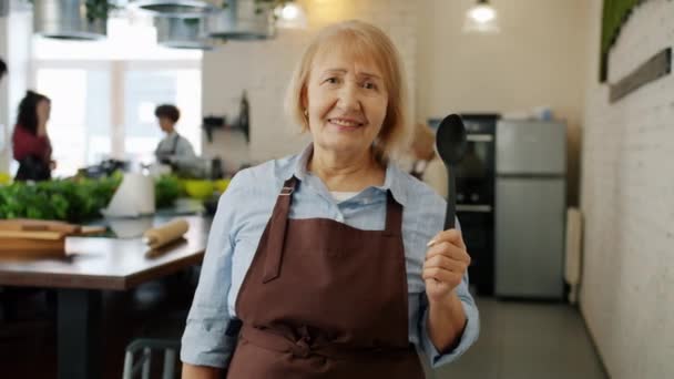 Portrait of elderly lady wearing apron smiling in cooking class enjoying education - Filmati, video