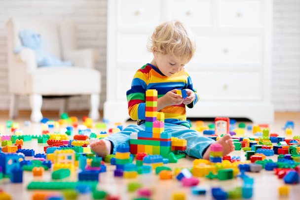 Child playing with colorful toy blocks. Little boy building tower at home or day care. Educational toys for young children. Construction block for baby or toddler kid. Mess in kindergarten play room. - Fotó, kép