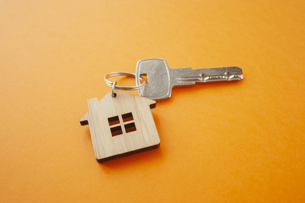 Key and house shaped keychain arrangement on orange background. Top view, flat lay. Real estate, insurance concept, mortgage, buy sell house, realtor concep - 写真・画像
